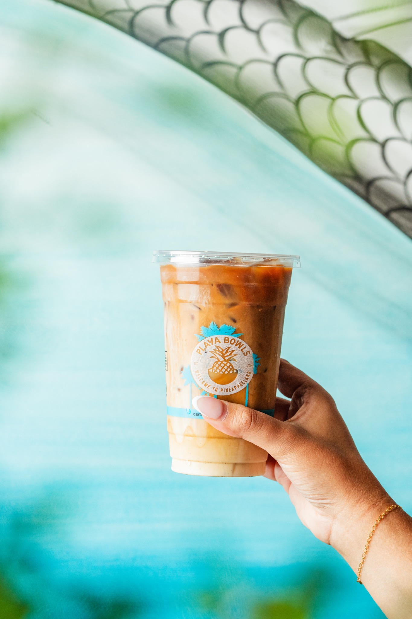 A hand holding Playa Sweet Cream Cold Brew against a turquoise wall